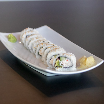 a california roll, served on a white plate, cut into 8 peices with ginger and wassabi on a black table top
